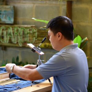 A man wearing a blue shirt works on a craft project at an indoor workshop setting.