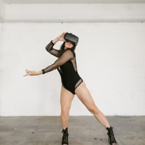 A woman in dance attire performs with a VR headset in an urban studio setting.